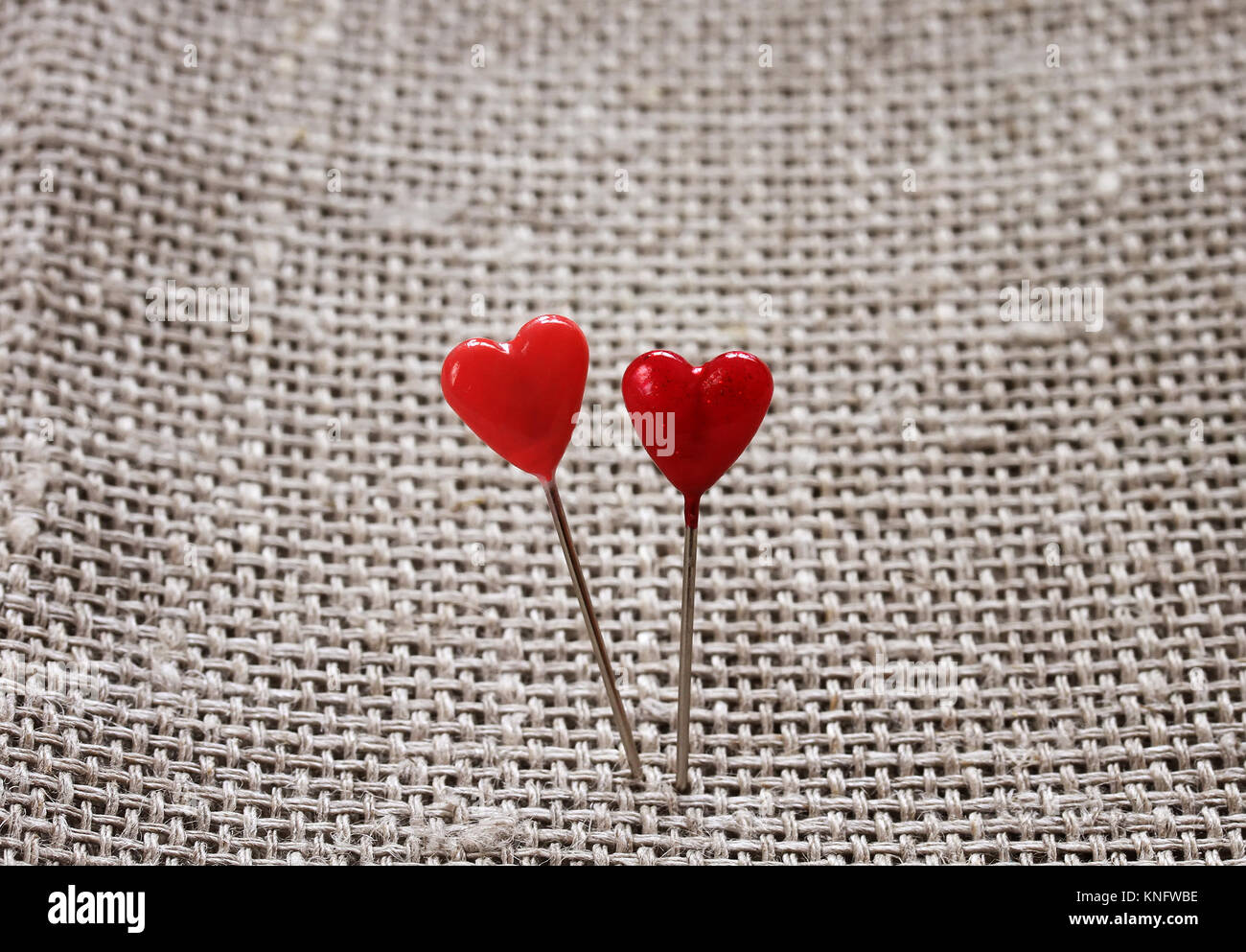 a pair of sharp pins in the form of red hearts stuck in the rough burlap Stock Photo