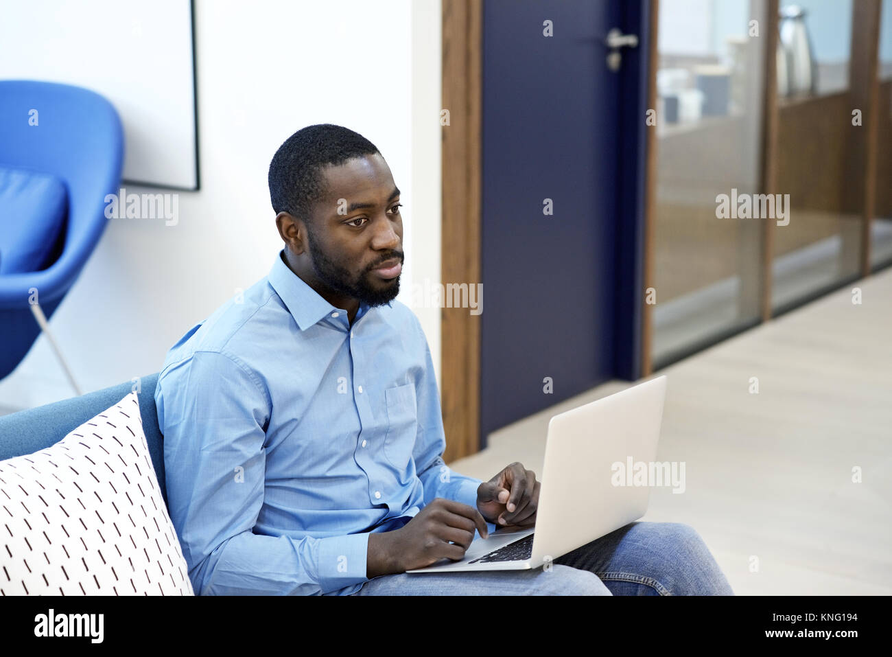 Black male creative professional listening to colleagues and using a laptop during a business meeting in a contemporary office Stock Photo