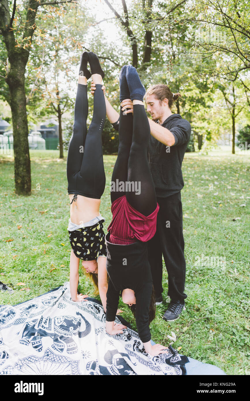 Handstand Outside Man teaching two young girls how to handstand outdoor in a park in ...