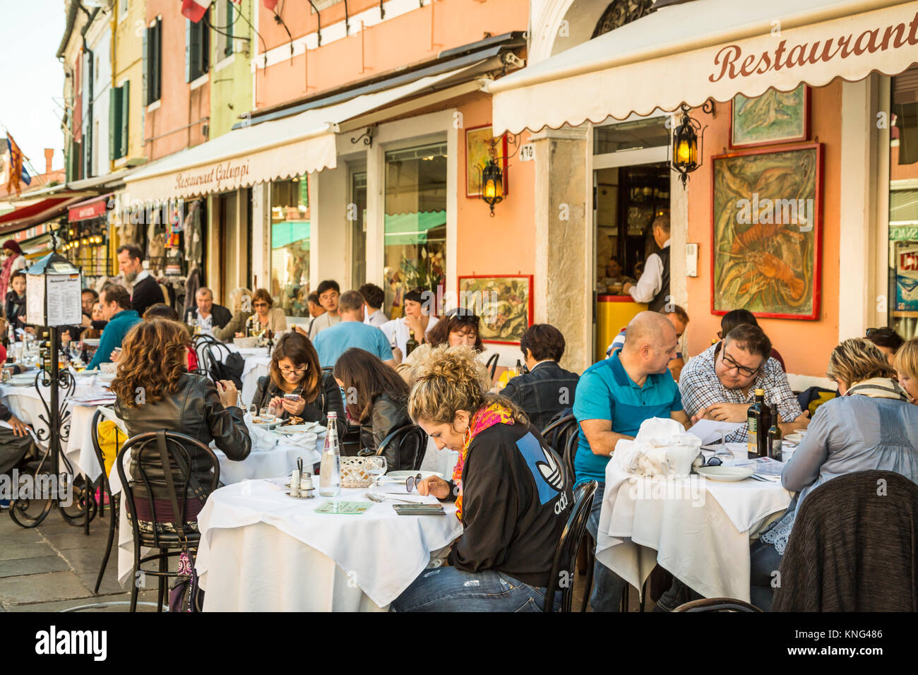 People eating at an outdoor restaurant in the Venetian village of Burano, Venice, Italy, Europe. Stock Photo