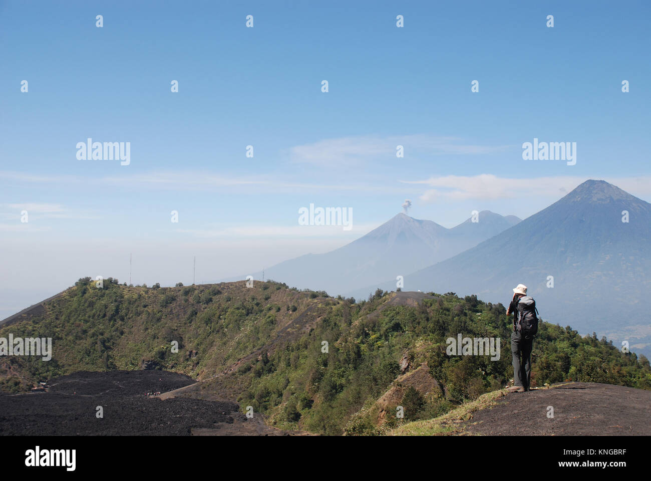 A trekker stands on the slopes of Pacaya volcano in Guatemala with Agua and Fuego volcanoes in the background Stock Photo