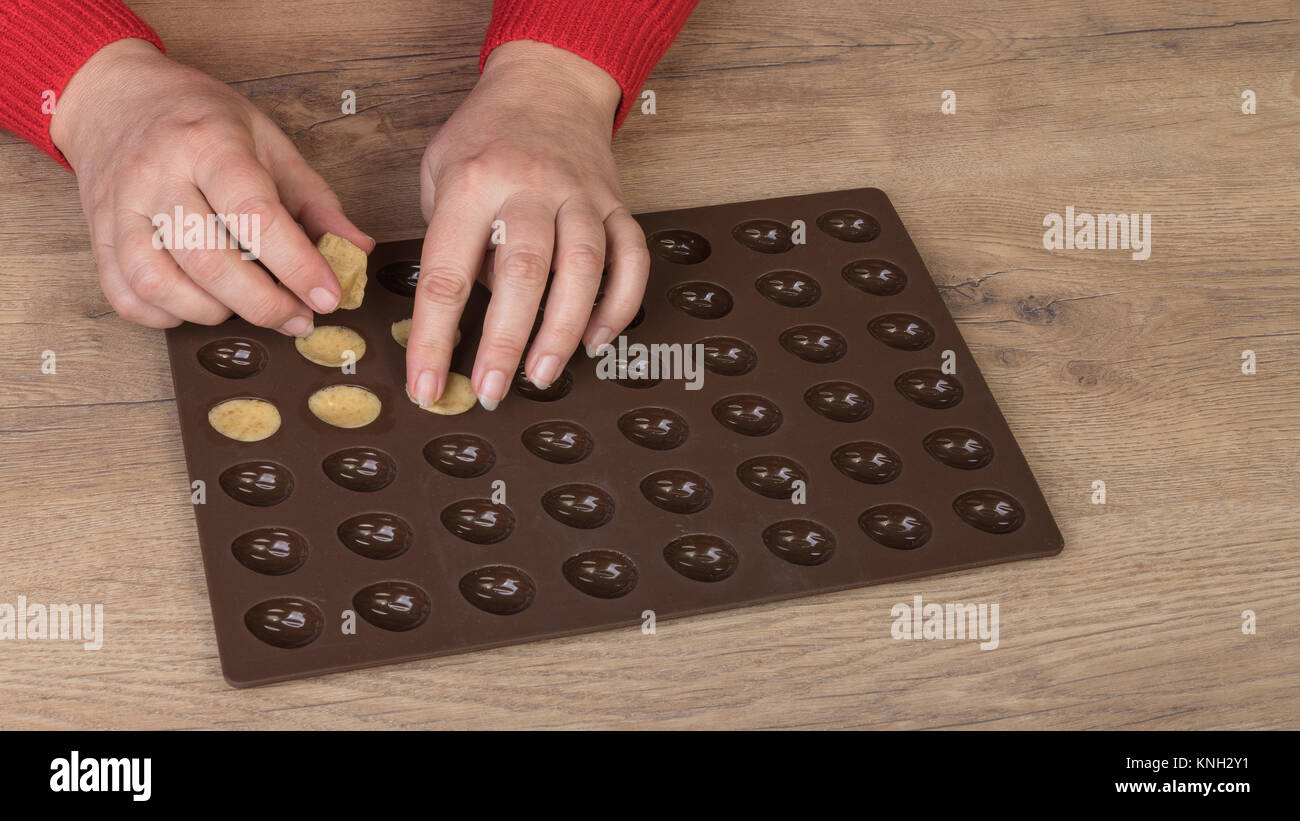 Making of Christmas nuts from shortcrust dough. Female hands filling a dough into brown silicone mold with wood background. Stock Photo