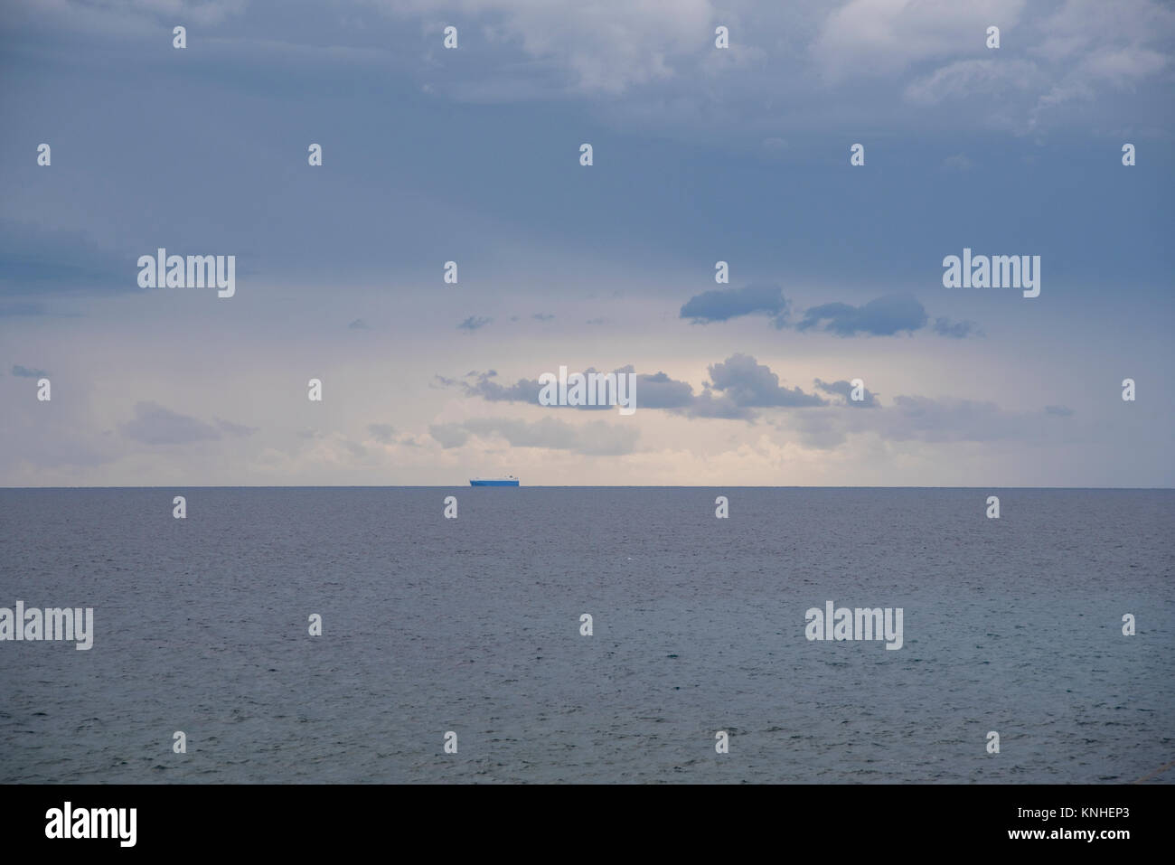 Cargo ship on the horizon under a cloudy sky, on the Mediterranean sea ...