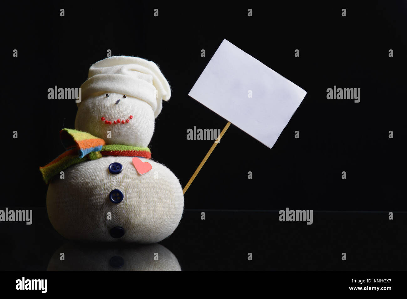 Snowman figure on a black background holding an empty placard board with stick attached. A contrasty low key photograph. Stock Photo