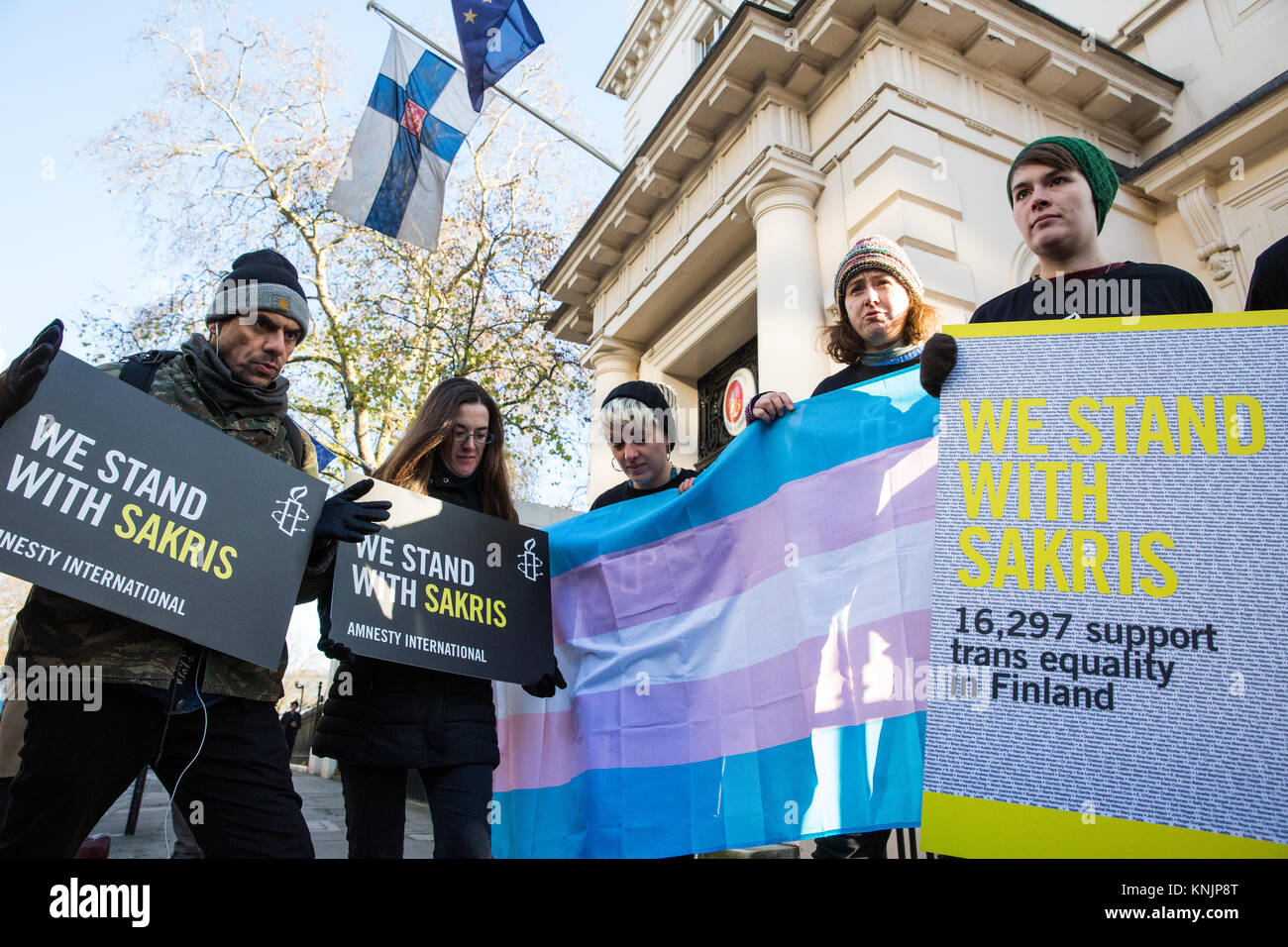 London, UK. 12th December, 2017. Amnesty International activists with a Transgender Pride flag stand on a placard stating 'Trans Act Finland' during a protest outside the Finnish embassy to call for revision of Finland’s ‘pre-historic’ trans sterilisation laws and in solidarity with Sakris Kupila, a 21-year-old Finnish human rights activist defending transgender rights and campaigning to change his country’s laws. Credit: Mark Kerrison/Alamy Live News Stock Photo