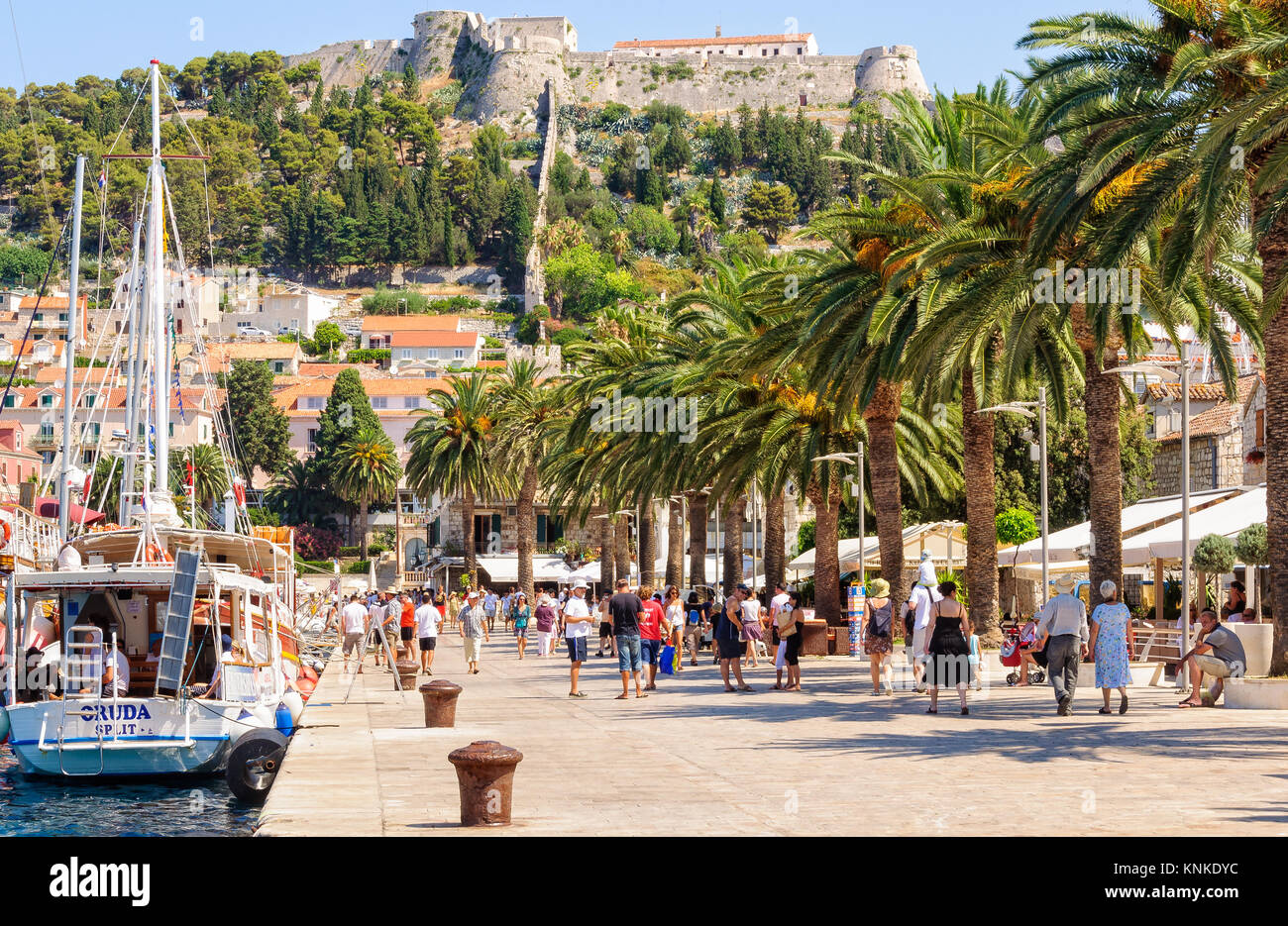 Tourists stroll in the  Riva harbour under the old Spanish fortress - Hvar, Croatia Stock Photo