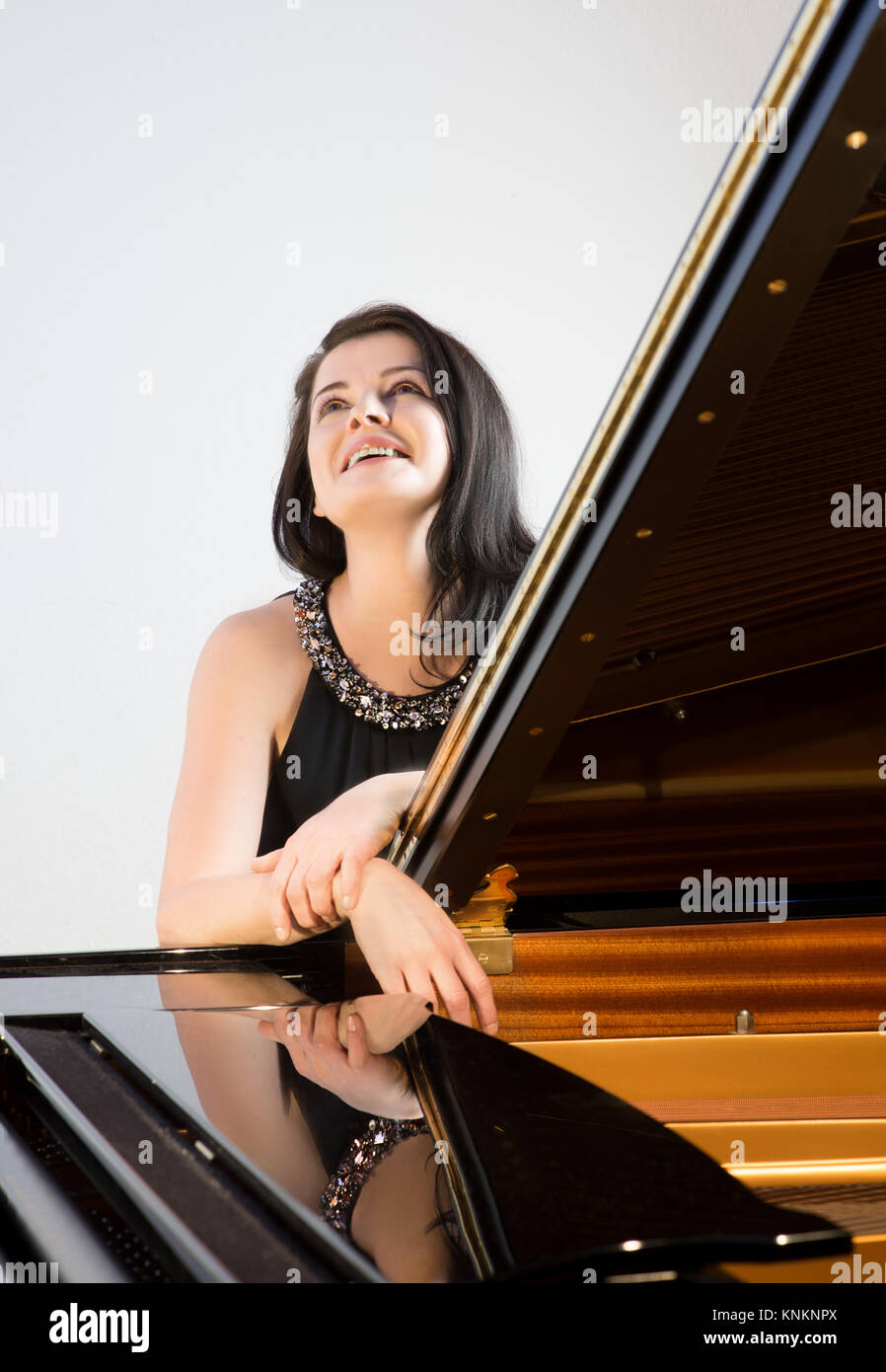 Smiling musician by grand piano looking up, text space Stock Photo