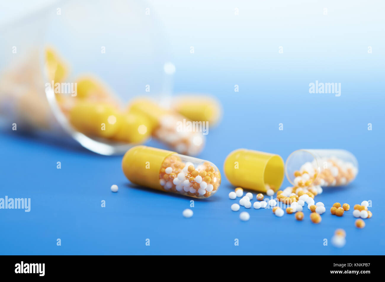 Splitopen yellow capsule on blue gradient background, more capsules