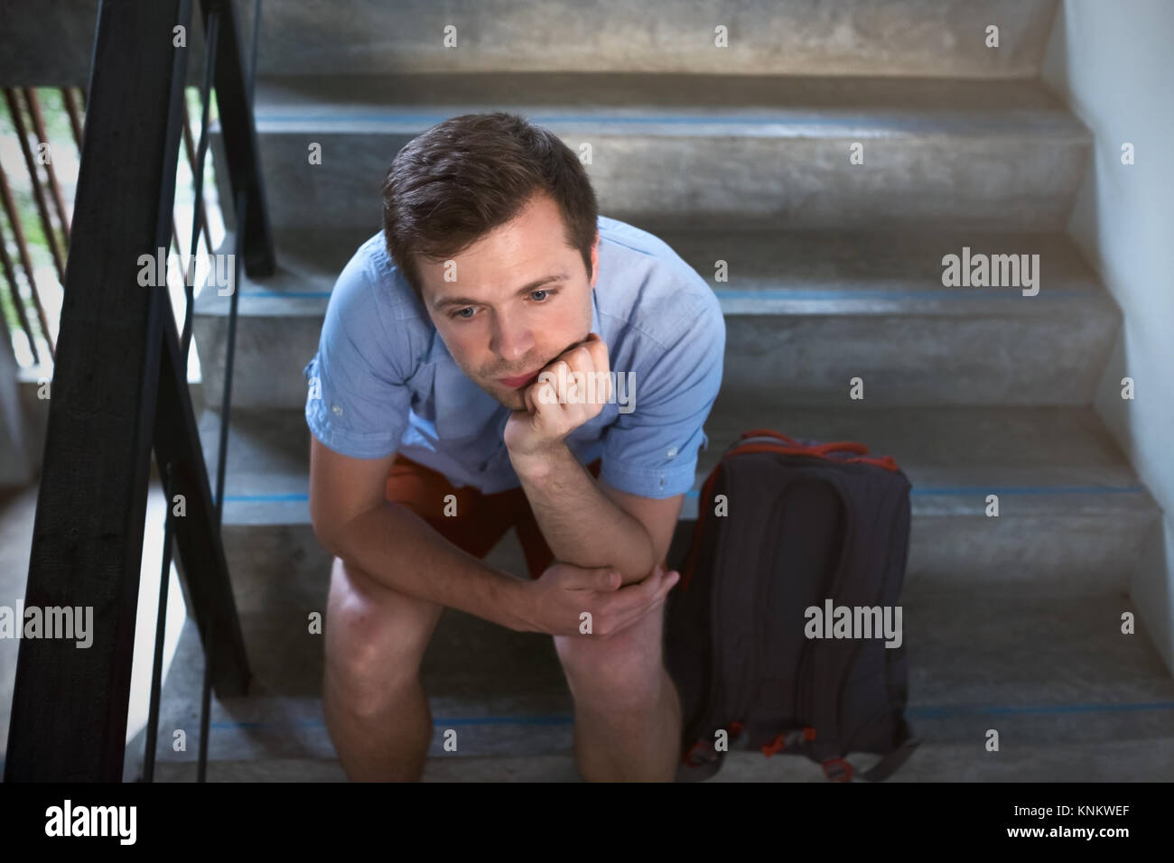 A young man is sitting on the stairs and sad. He lost the keys to the apartment, Stock Photo