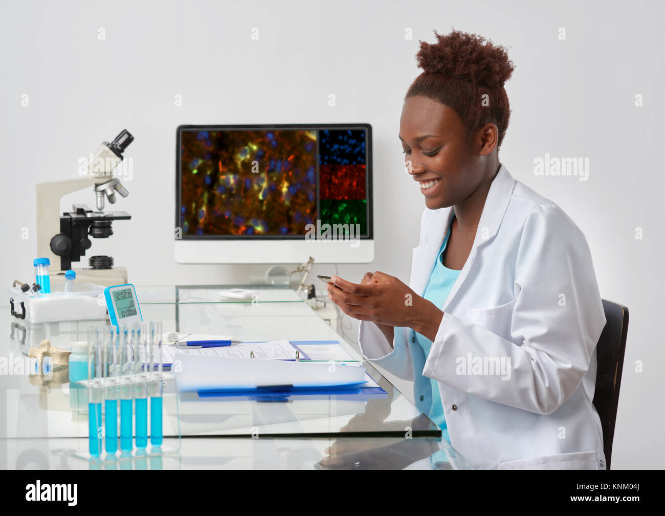 Happy young African scientist texting on her mobile phone in research facility. Stock Photo