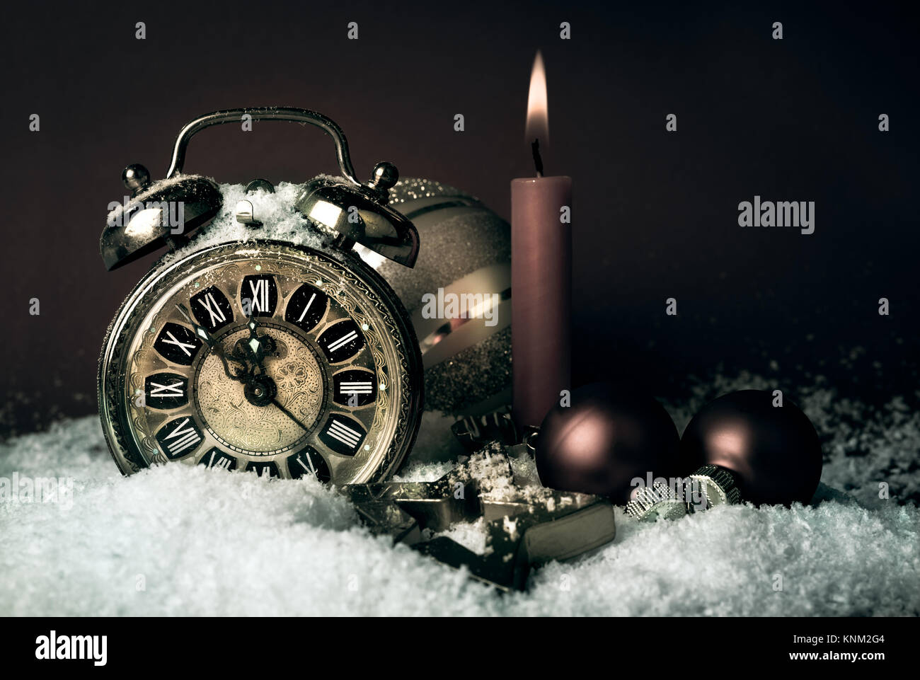 Old alarm clock showing five to midnight and a candle on a New Year's