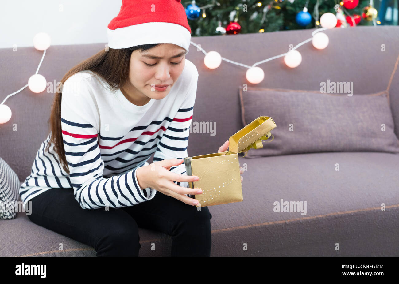 Asian woman upset when open gold xmas gift box at holiday party on sofa,boredom Christmas party present Stock Photo