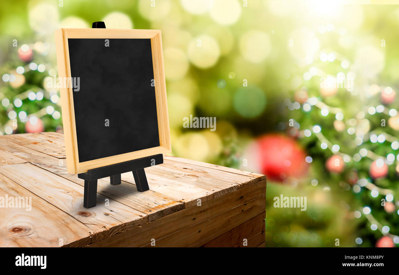 Blackboard with easel on wood table ( food stand ) at blur Christmas tree bokeh light background,Template mock up for display or montage of product or Stock Photo