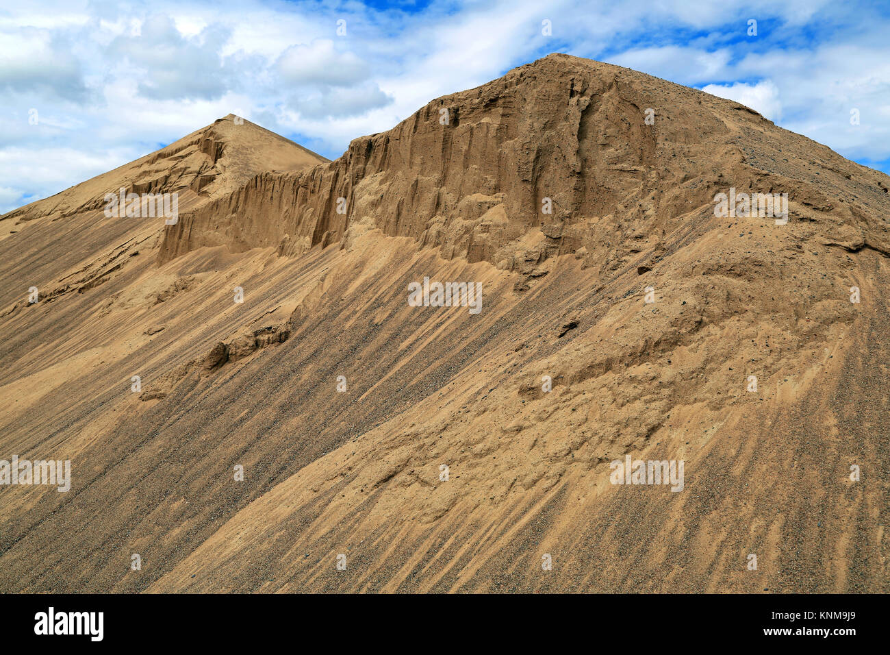 Hills of construction sand against blue sky and few white clouds. Stock Photo
