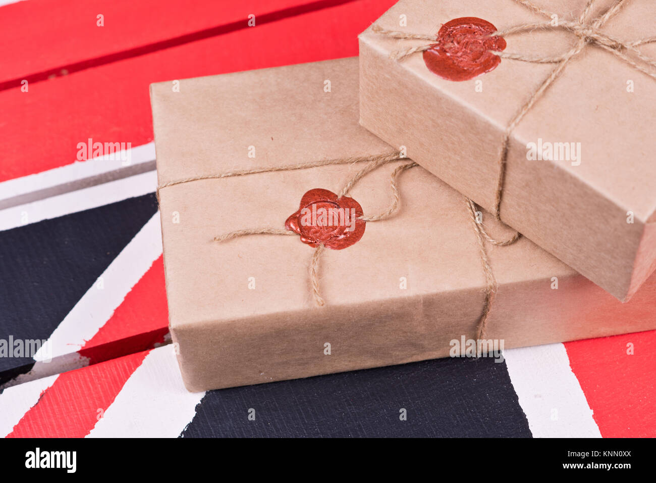 Boxes, wrapped into craft paper, fixed with packthread with a wafer on a background of a wooden candlestick on a coloured wooden desk. Stock Photo