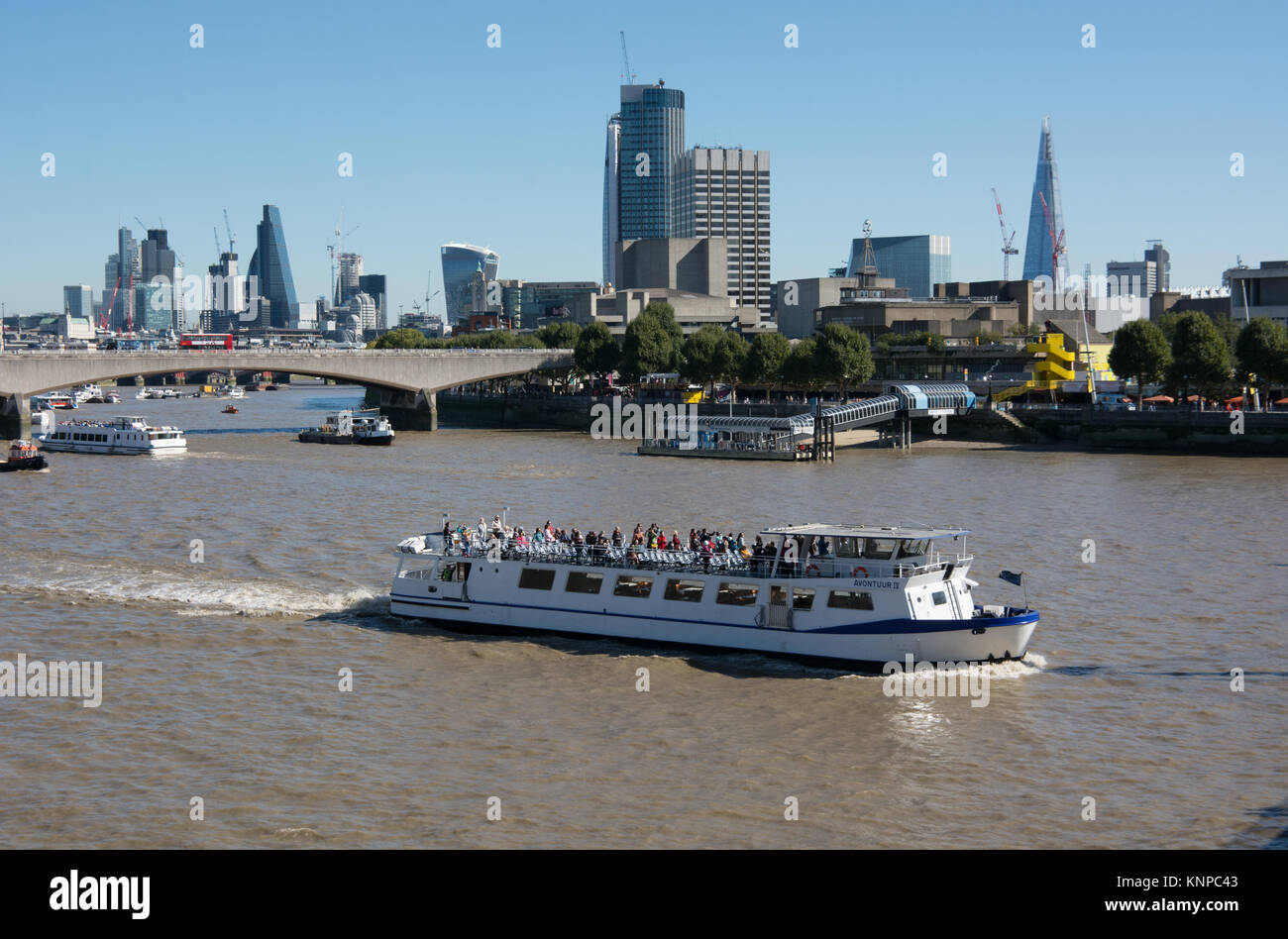 A tourists sightseeing cruise sails along the River Thames . In the background is Waterloo bridge and the City of London Skyline Stock Photo