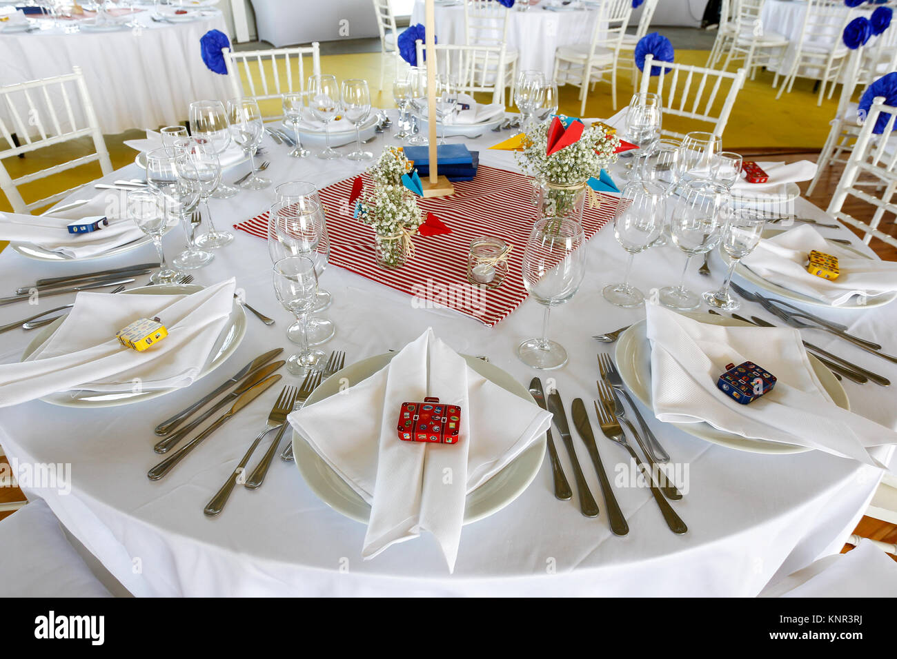 Circle dinner table served with white crockery and decorated with colorful objects. Stock Photo