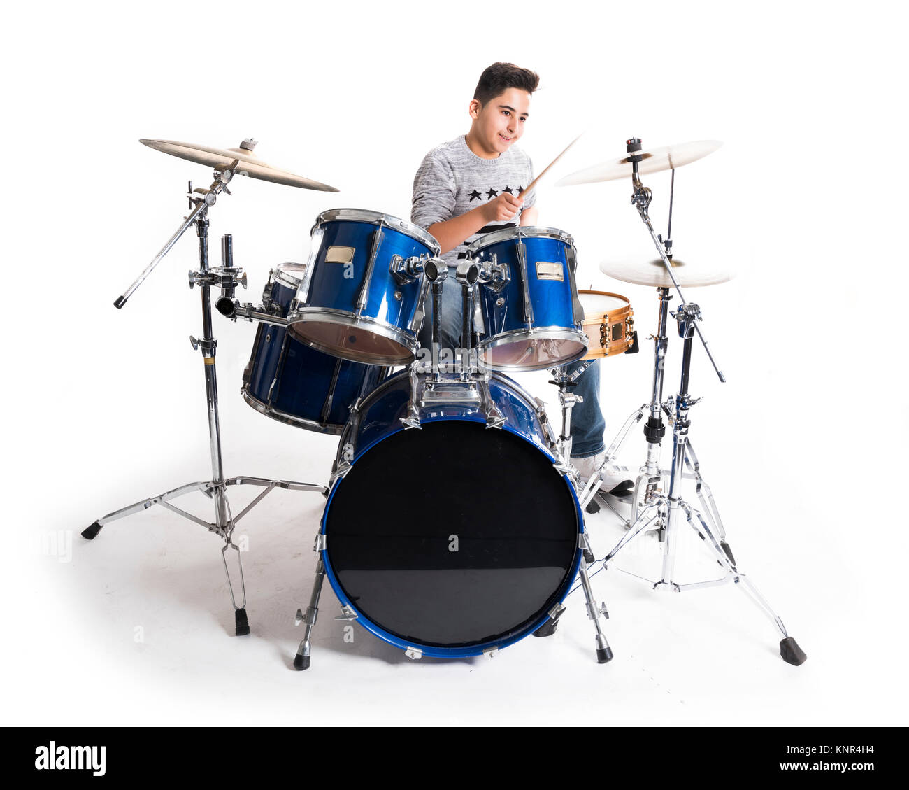 teen boy at drumset in studio against white background Stock Photo
