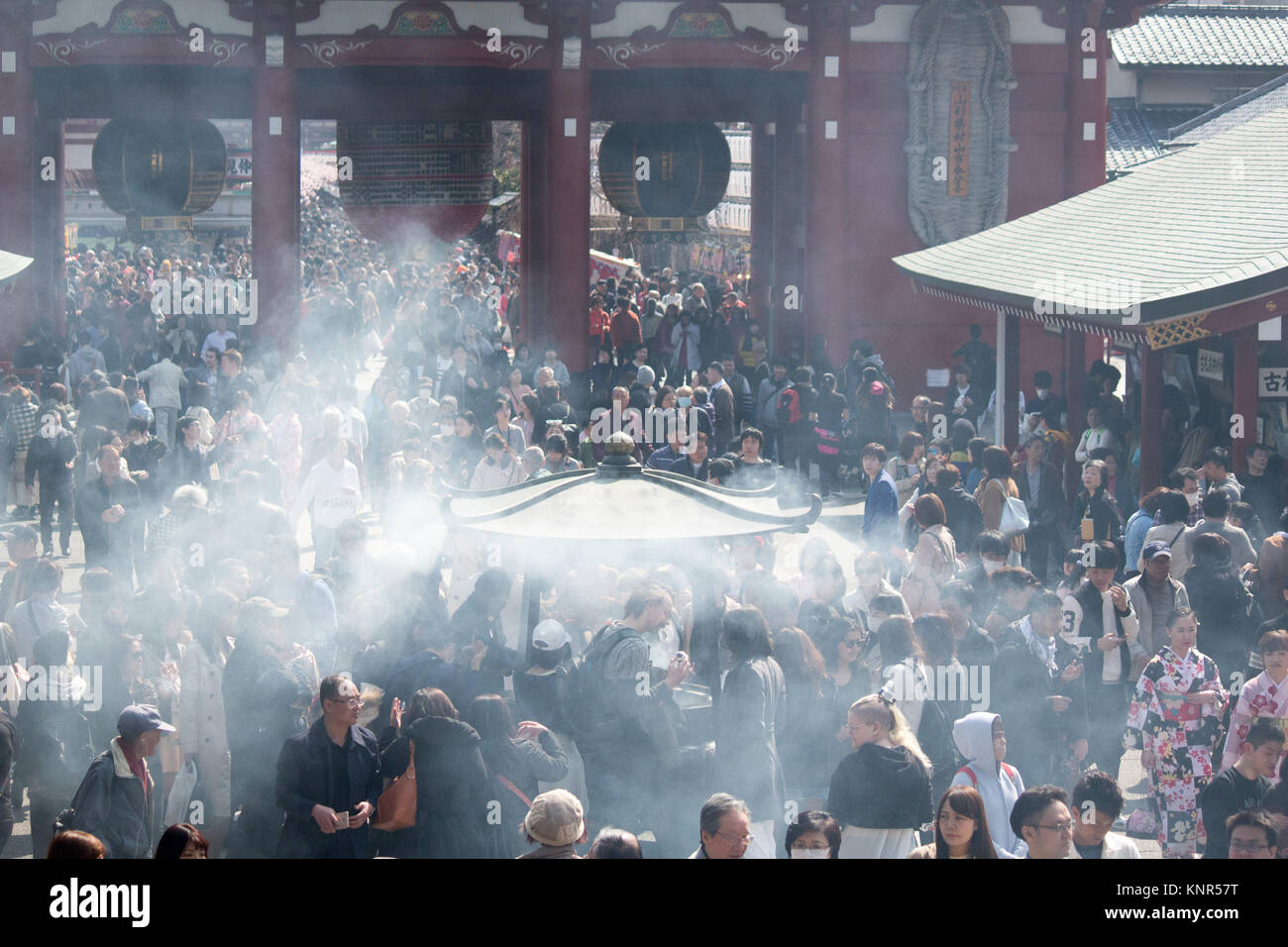 Burning incense causing large clouds outside the  Sensō-ji, historic Buddhist Temple in Tokyo packed with people. Stock Photo