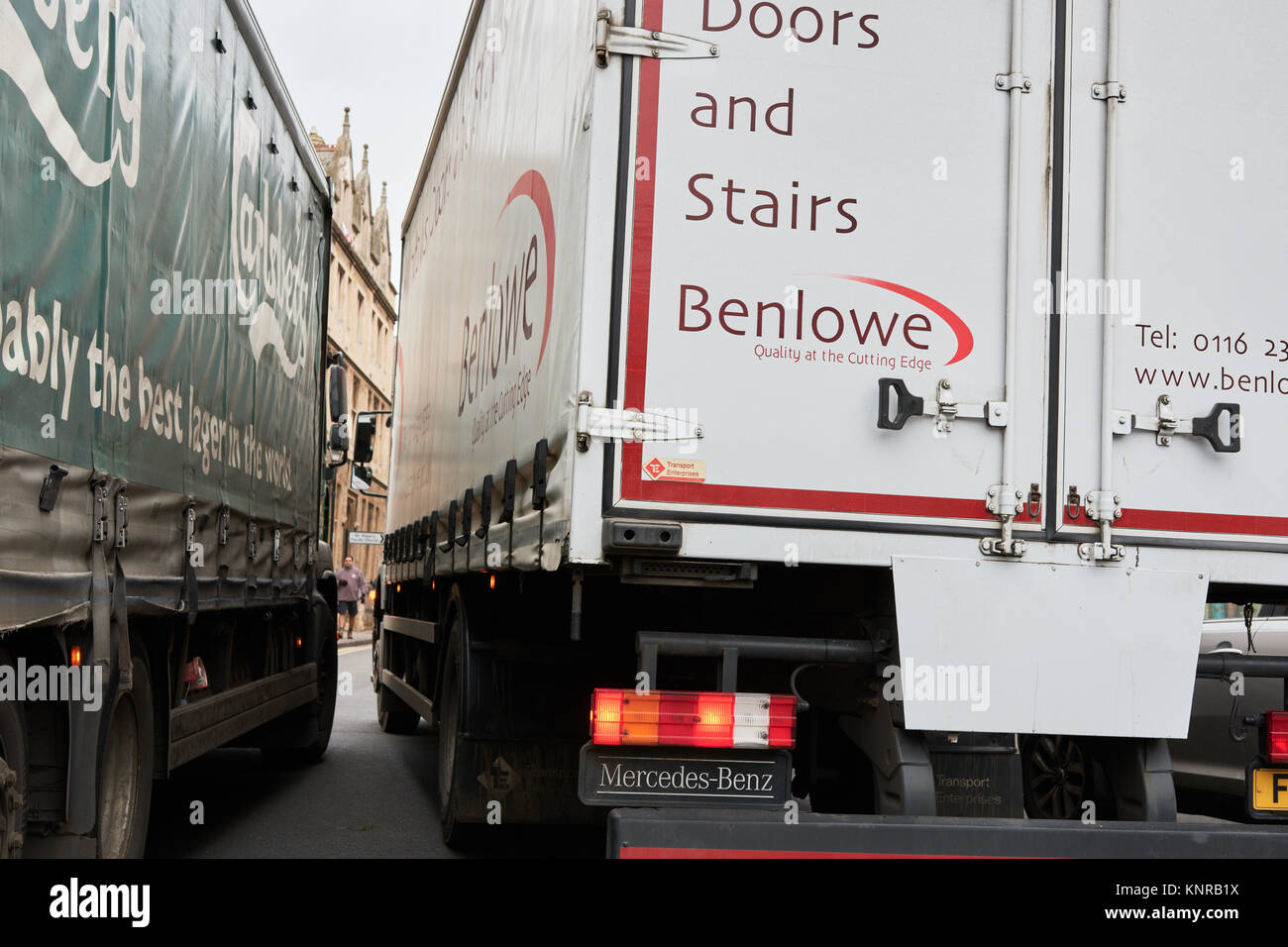 Narrow squeeze as a lorry attempts to pass between a parked lorry and cars along New Street in the country town of Oundle, Northamptonshire, England. Stock Photo