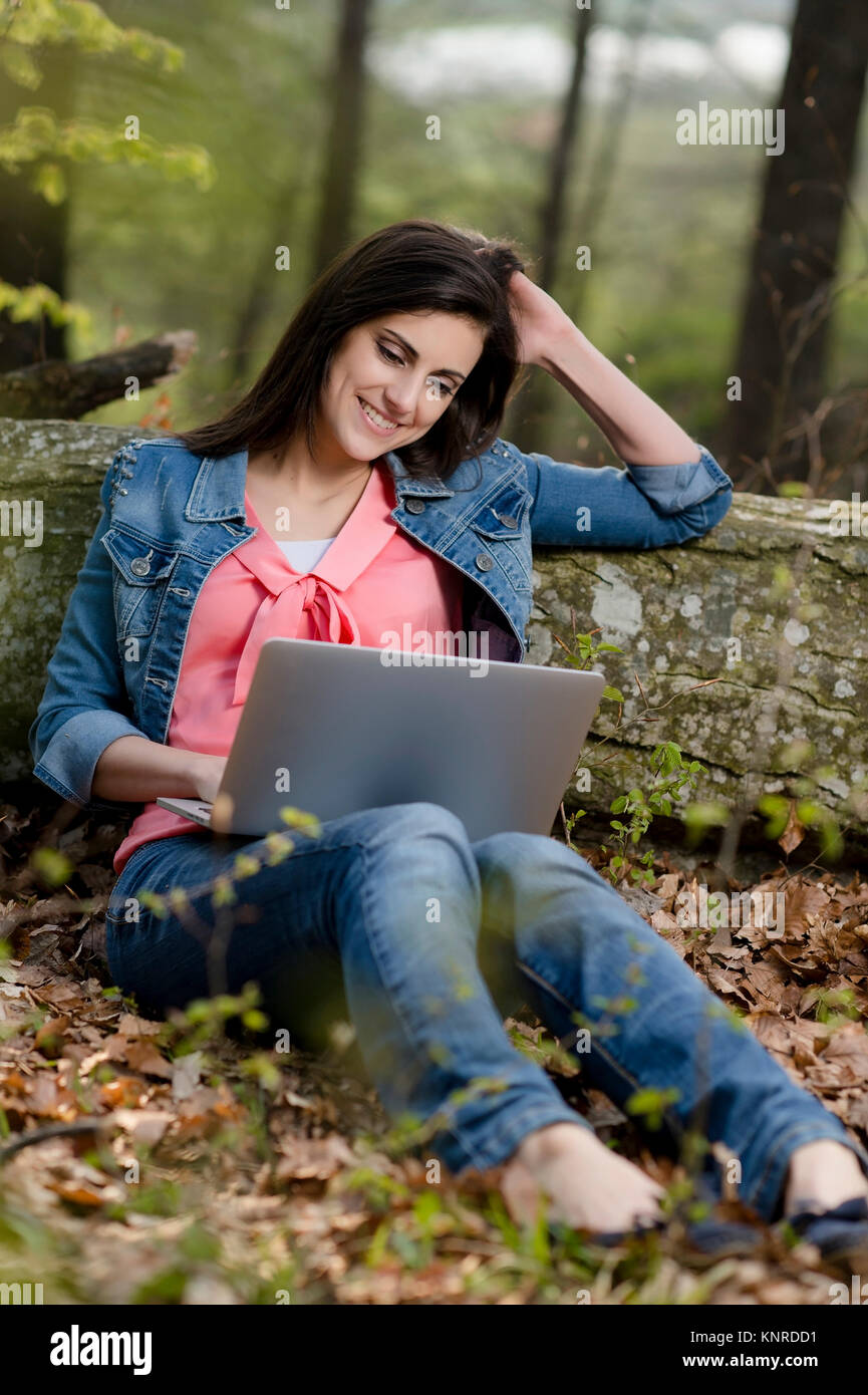 Junge Frau sitzt mit Laptop auf Laubboden im Wald - woman with laptop in nature Stock Photo