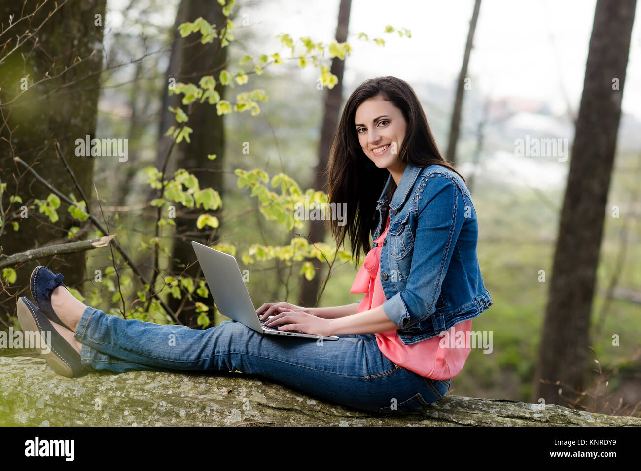 Junge Frau sitzt mit Laptop auf einem gefaellten Baumstamm - woman with laptop in nature Stock Photo