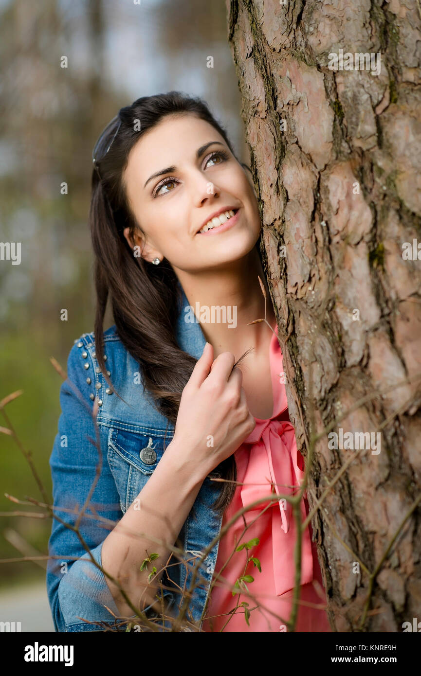 Junge Frau steht neben Baumstamm - woman is standing next to tree trunk Stock Photo