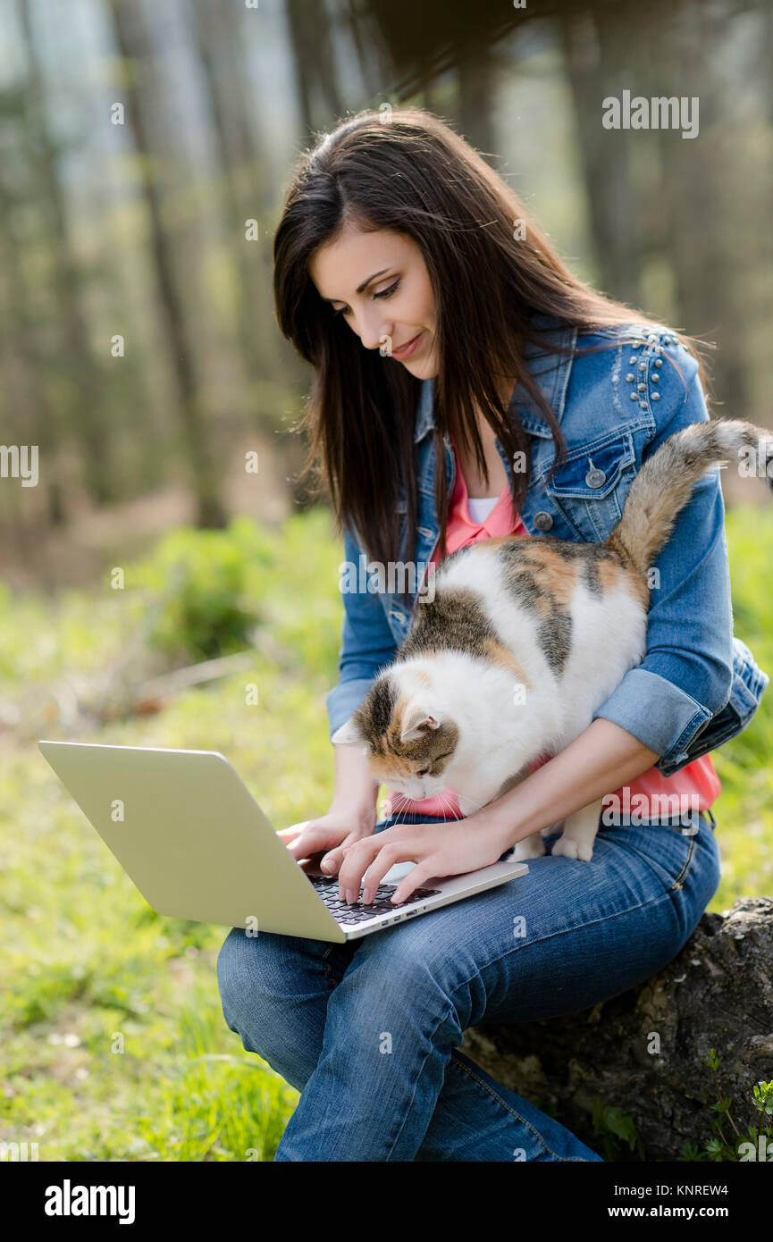 Junge Frau mit Katze sitzt mit Laptop in der Natur - woman with cat and laptop in nature Stock Photo