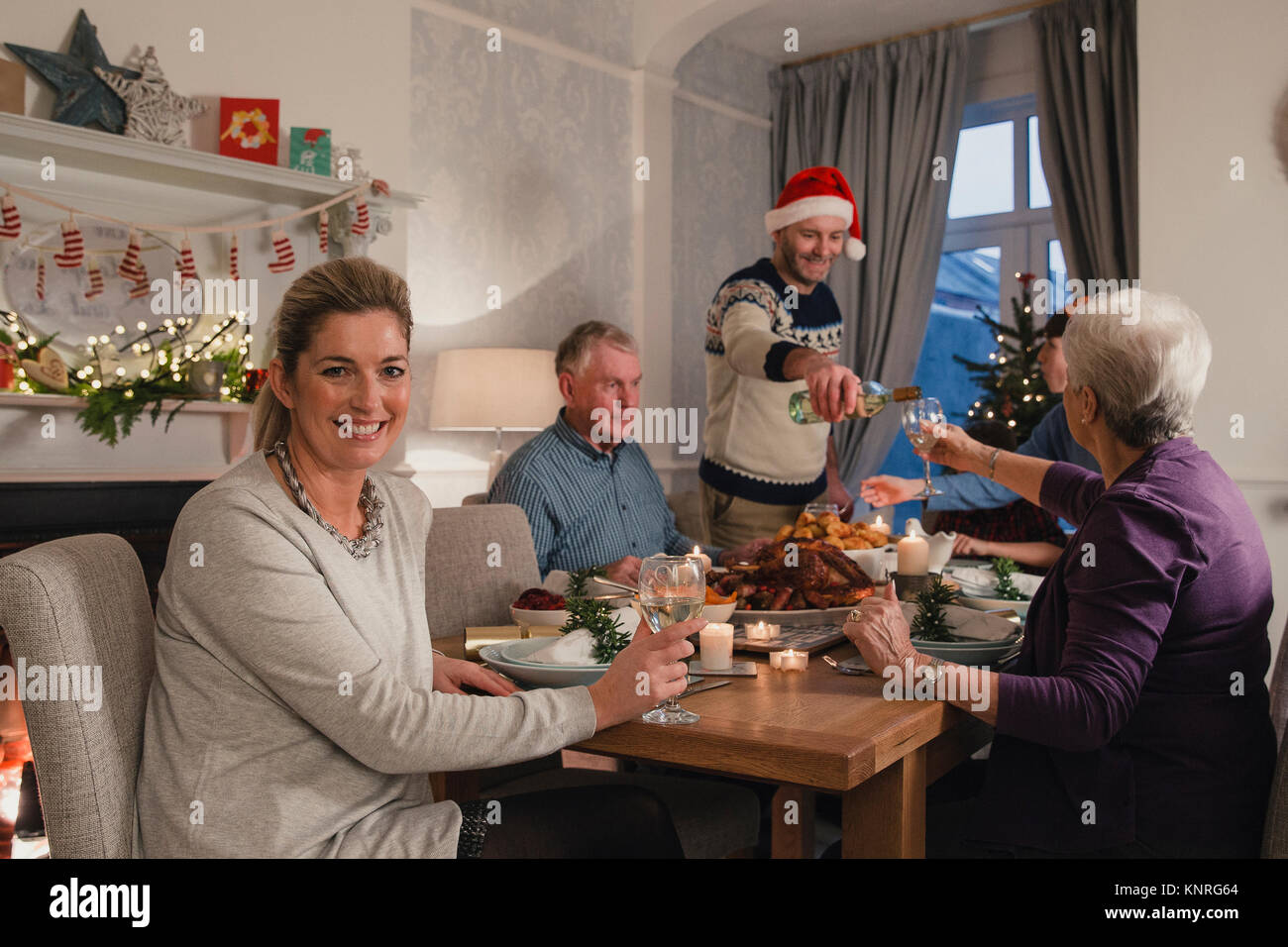 Happy mature woman is smiling for the camera while enjoying a glass of wine at her family christmas dinner. Stock Photo