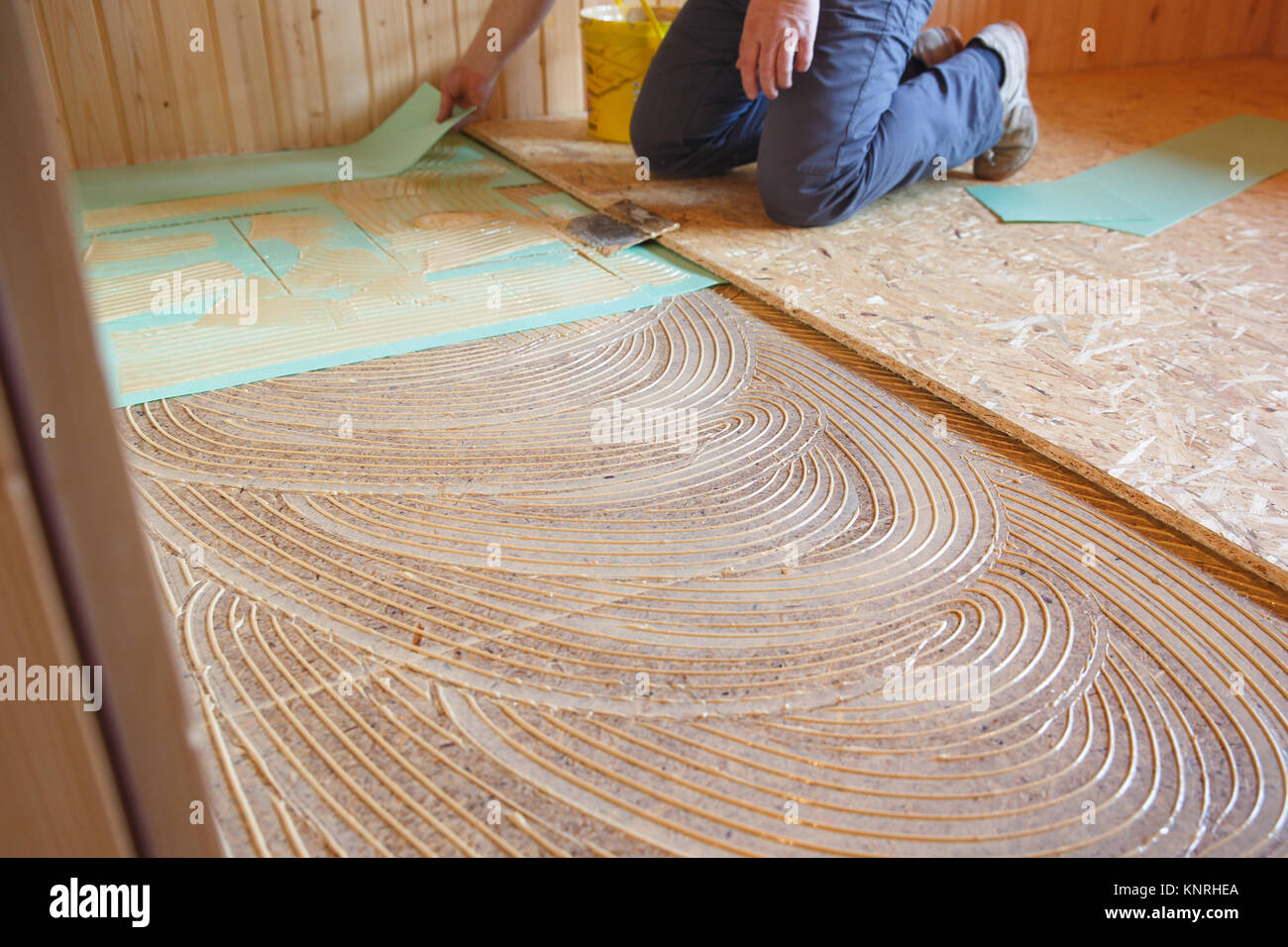 Worker laying insulation layer and adhesive primer spread on the old floor, prepared for laying of new flooring. Professional work, home improvement a Stock Photo