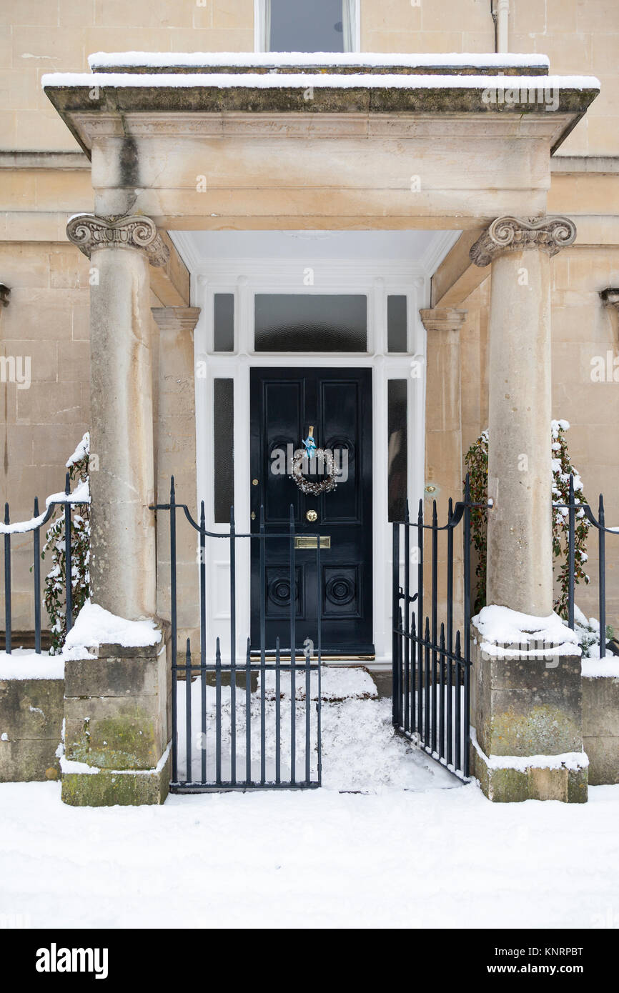 Stone portico entrance covered in snow leading to a traditional door with a Christmas wreath. Stock Photo