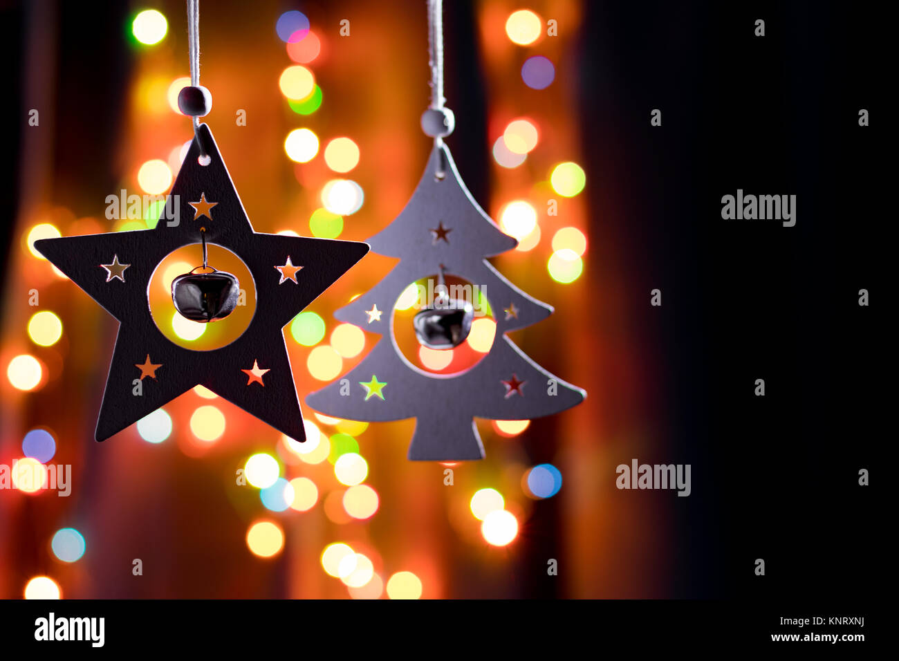 Handmade christmas decorations, star and fir tree with small round bells on dark background with colorful bokeh lights Stock Photo