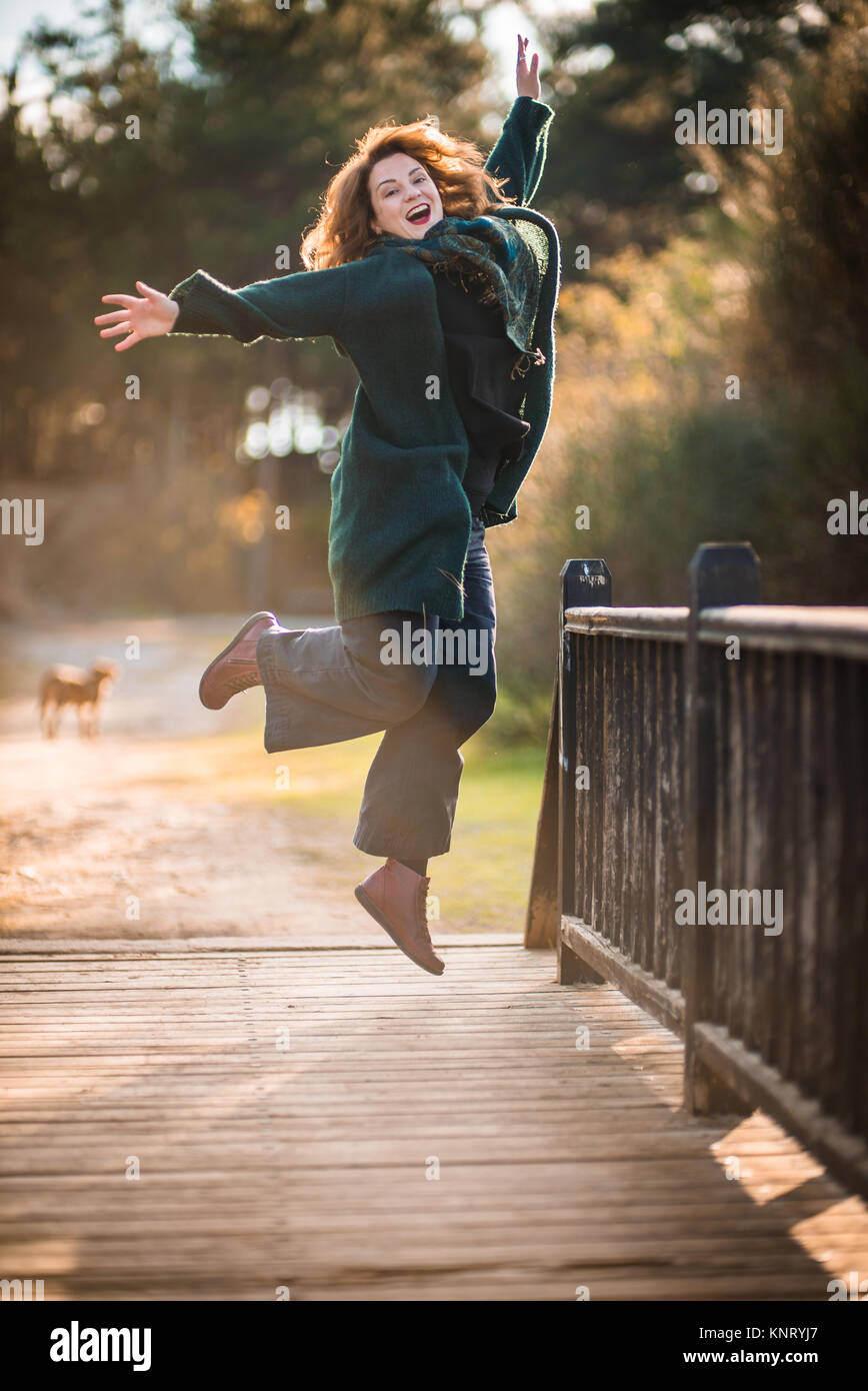 Atractive Happy Woman Jumping Up by a Wooden Old Bridge in the Forest, Enjoying Life Stock Photo