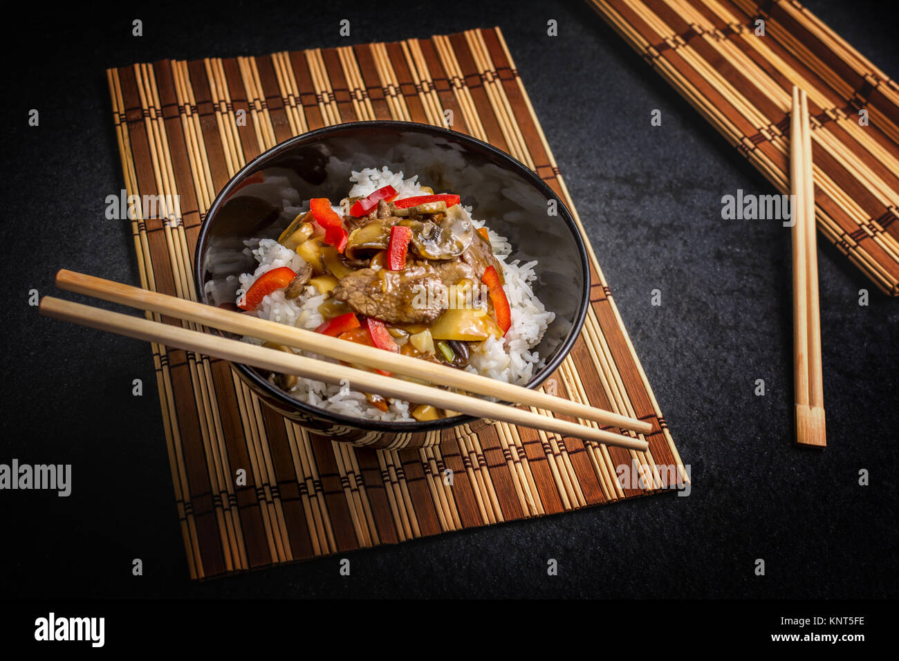 Asian rice with beef in black plate with chopsticks on dark stone table Stock Photo