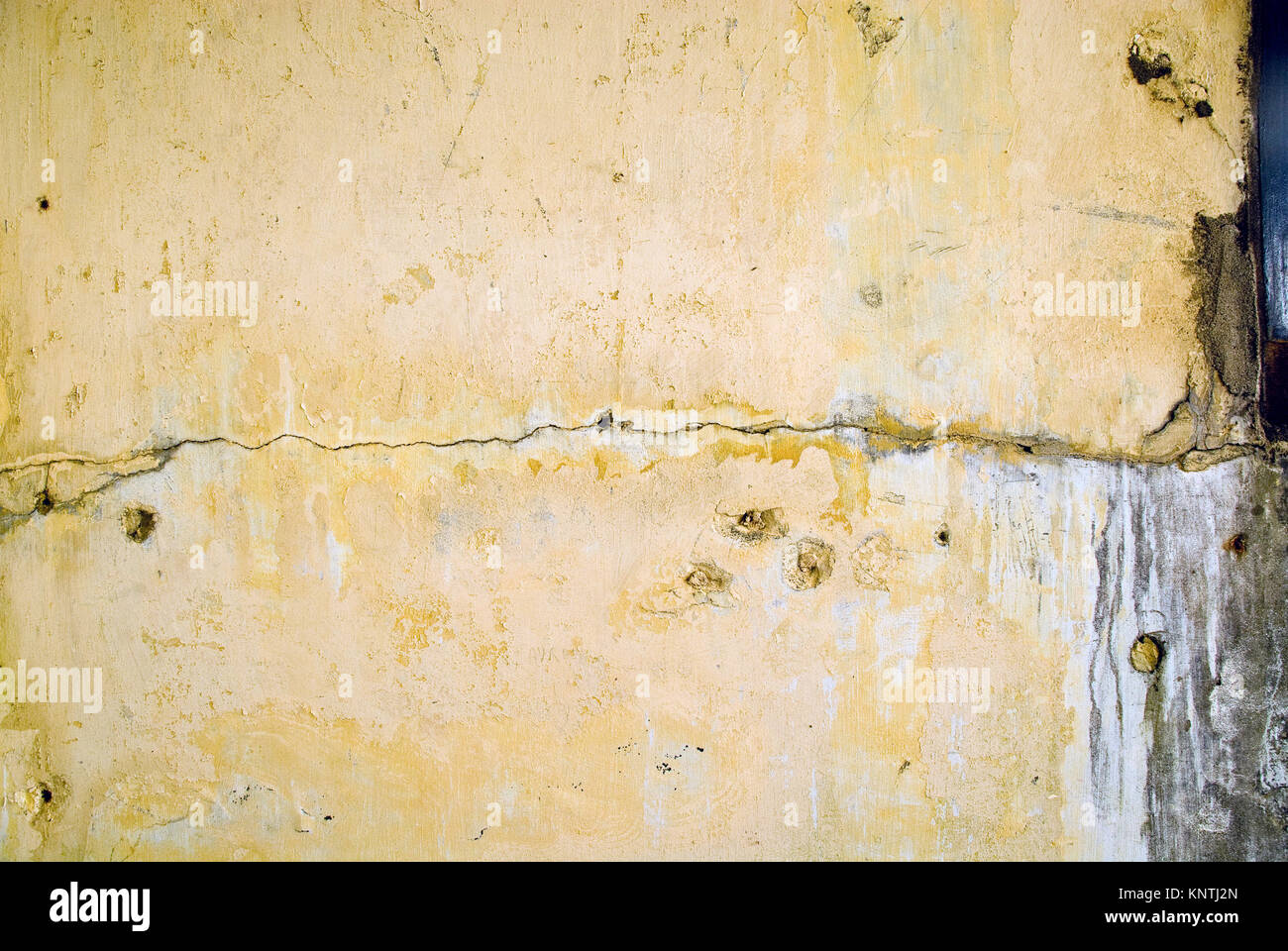 Yellow plastered wall with visible deterioration and cracks form an old