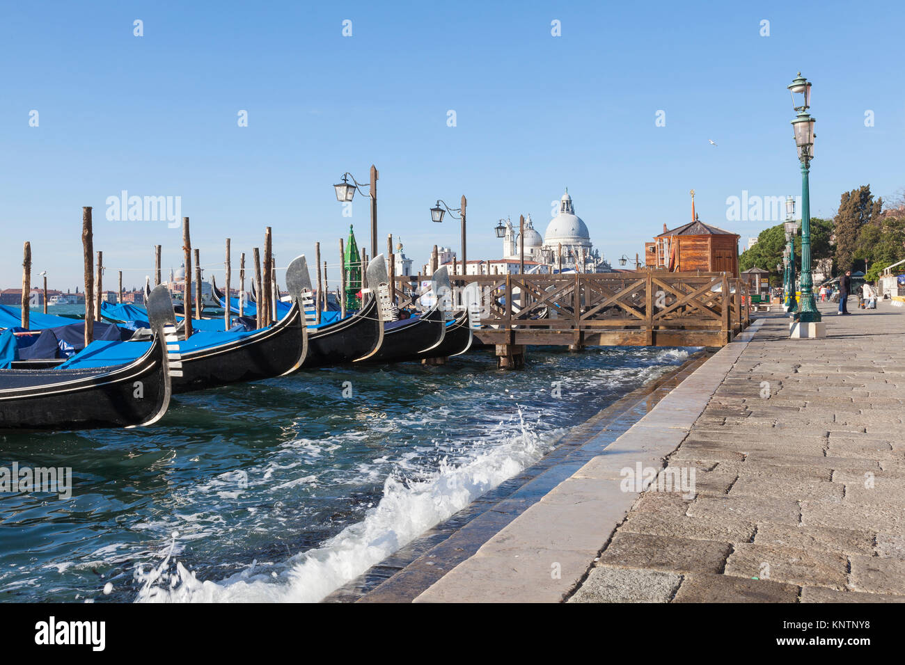 Gondolas with wave splash on an Acqua Alta high  tide, San Marco, Venice, Italy looking along the row of ferros or metal ornaments on the prow Stock Photo