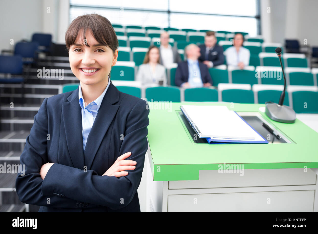 Portrait of young businesswoman with arms crossed smiling in lecture hall Stock Photo