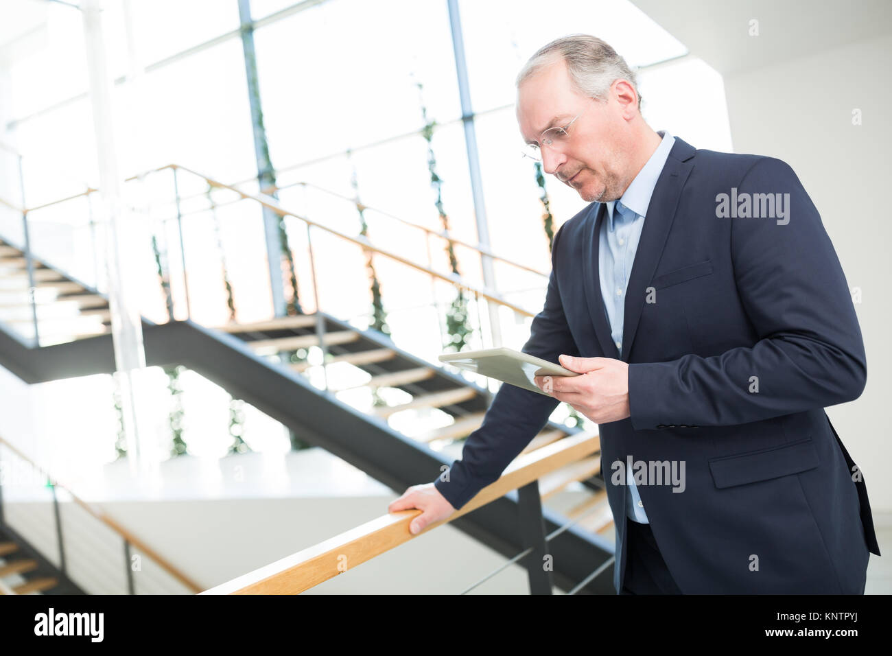 Senior businessman using tablet computer while leaning on railing in ...