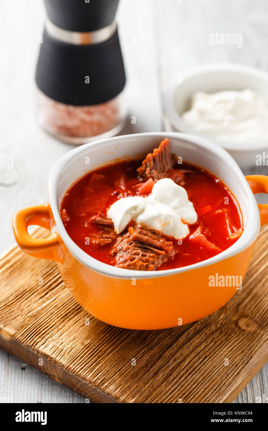 Traditional soup of Russian and Ukrainian cuisine borsch. Meat soup with beets in an orange bowl on a light wooden background. Stock Photo