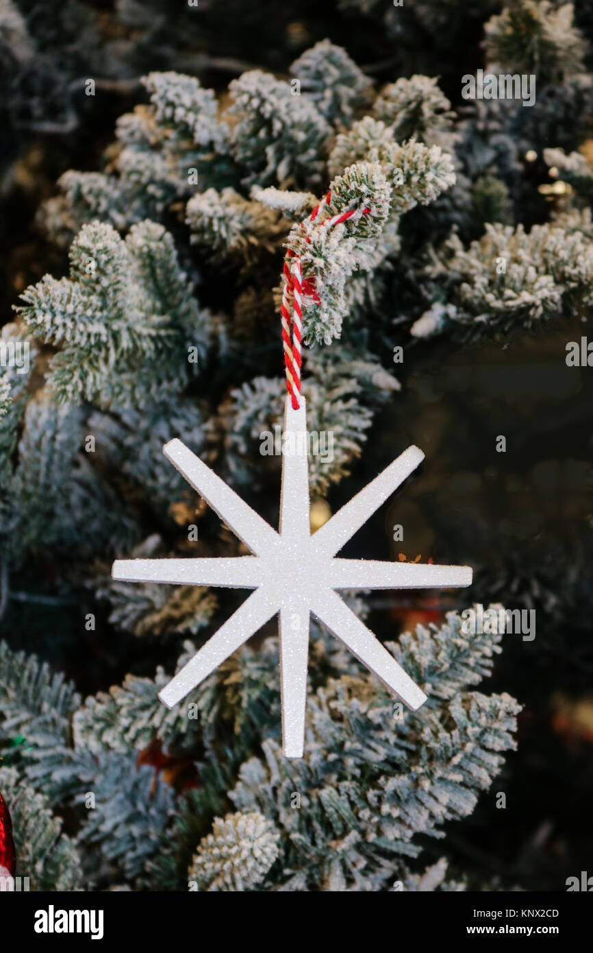 Stylized simple snowflake ornament with sparkles hanging on a flocked Christmas tree Stock Photo