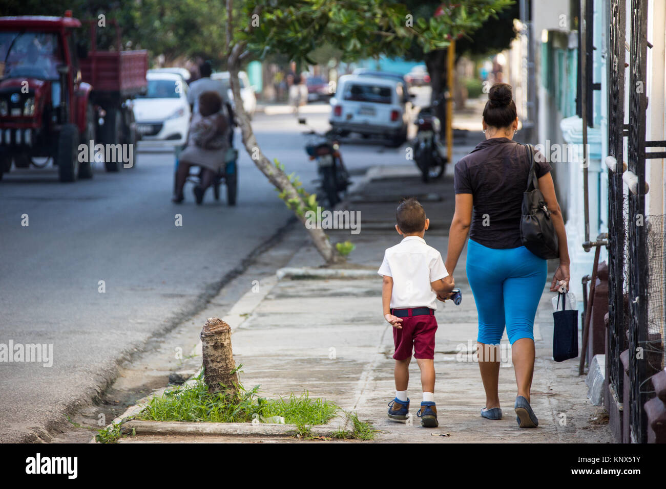 Local boy walking on the sidewalk with his mother, Cienfuegos, Cuba Stock Photo