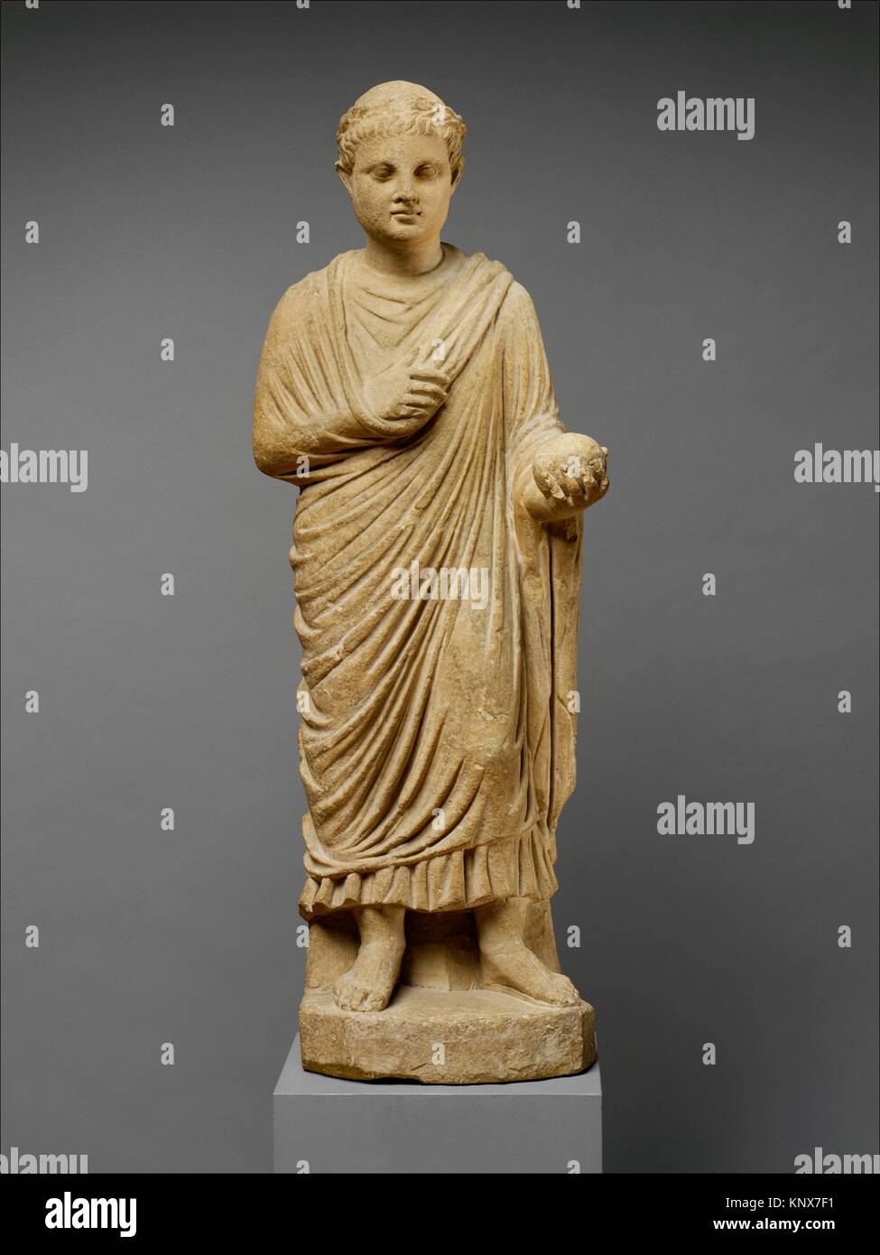 Limestone statue of a wreathed boy holding a ball or piece of fruit. Period: Hellenistic or Early Imperial; Date: 3rd century B.C.-1st century A.D; Stock Photo