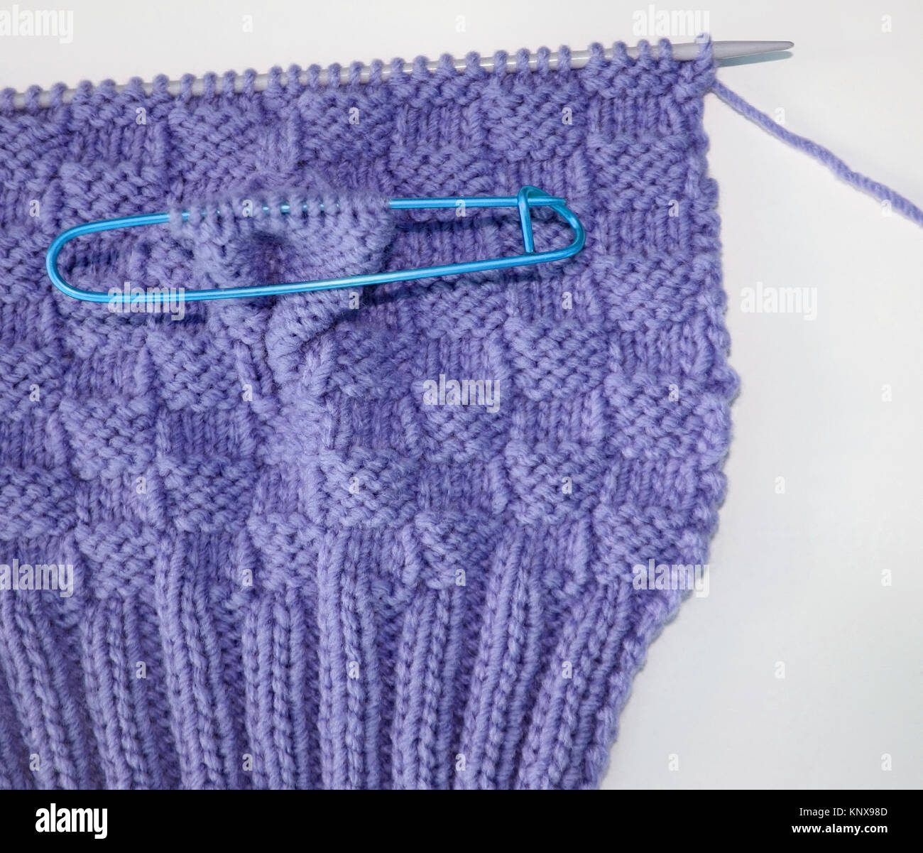 Basket weave pattern knitted on knitting needle in lilac color wool.   Stitch holder in place marking off extra stitches to be knit later Stock Photo