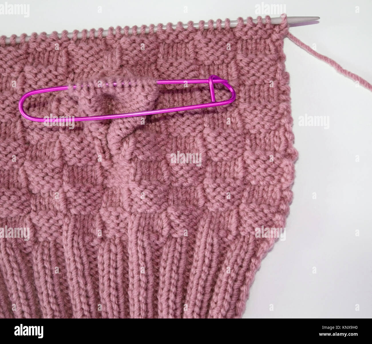 Basket weave pattern knitted on knitting needle in rose color wool.   Stitch holder in place marking off extra stitches to be knit later Stock Photo