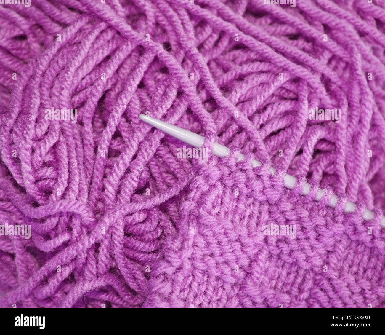 Knitted stitches on knitting needle with strands of lilac colored yarn in background Stock Photo