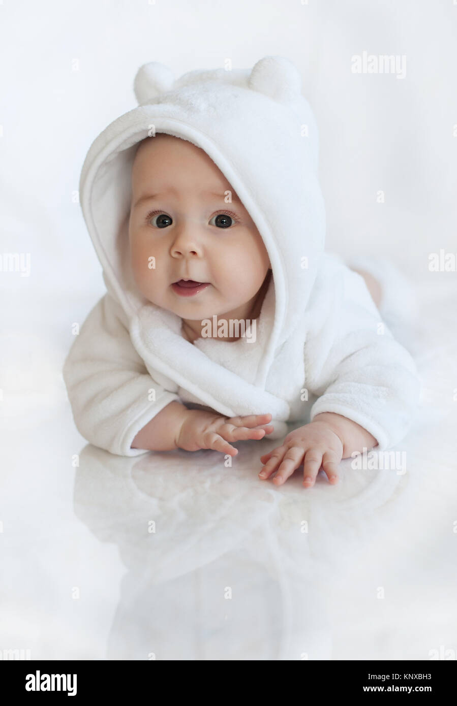 Portrait of baby girl wearing soft white hooded robe laying on stomach