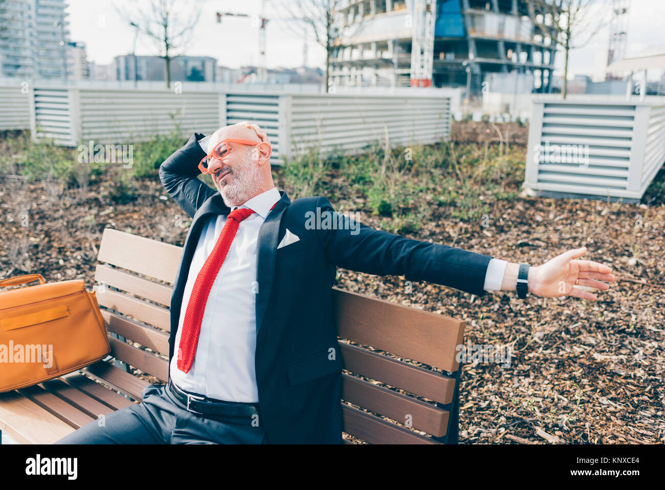 Middle-age contemporary businessman sitting outdoor on a bench in a ...