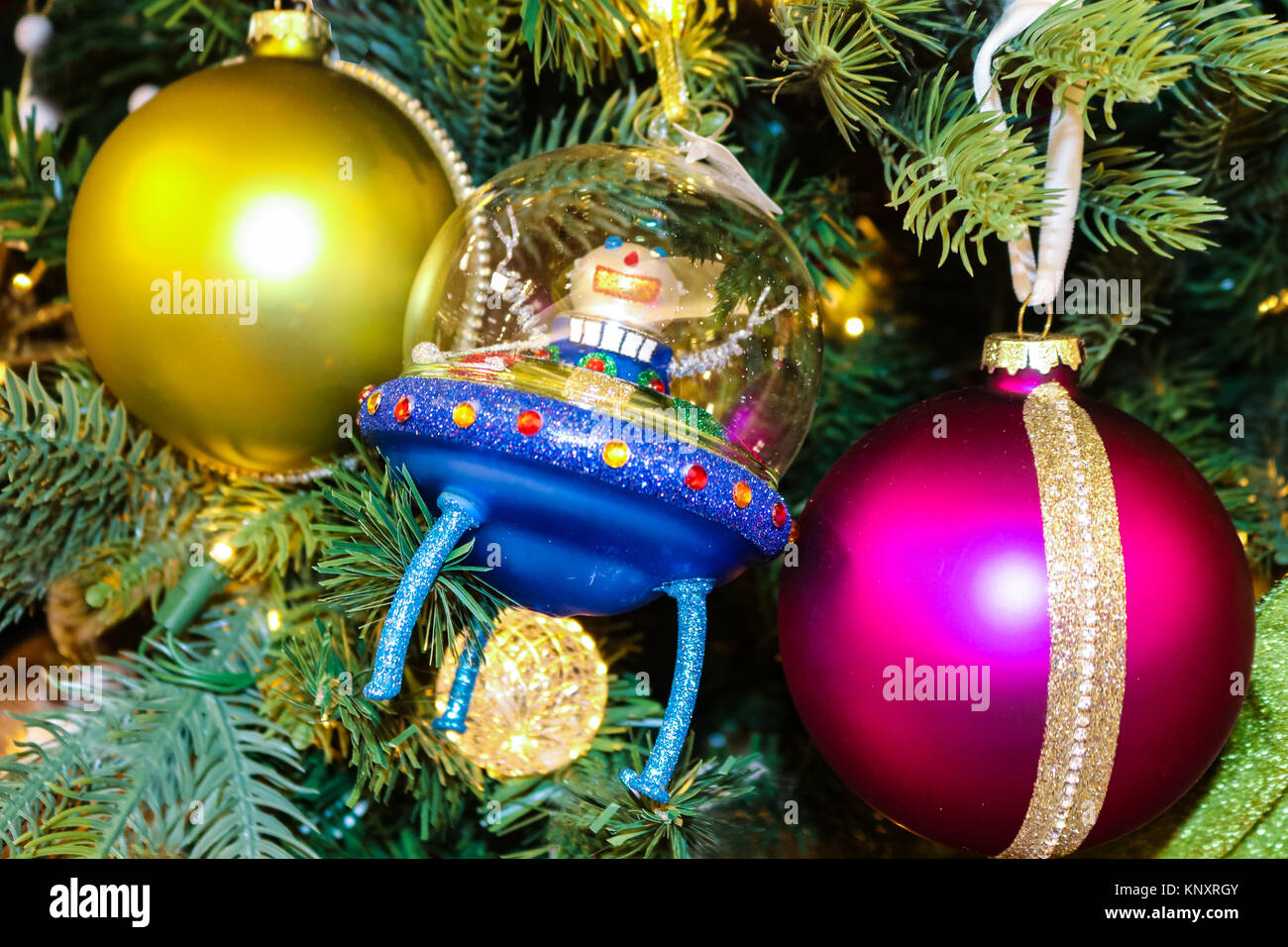 Spaceman giving peace sign in blue alien rocket on traditional Christmas tree with red and magenta ornaments Stock Photo
