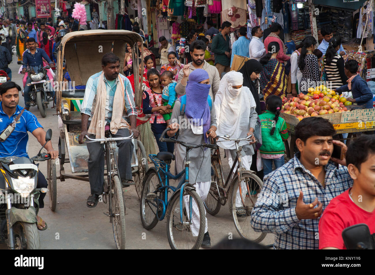 A rickshaw cyclist and two muslim women pushing bicyles through a busy and congested Dasashwamedha Ghat Road  in Varanasi, India Stock Photo