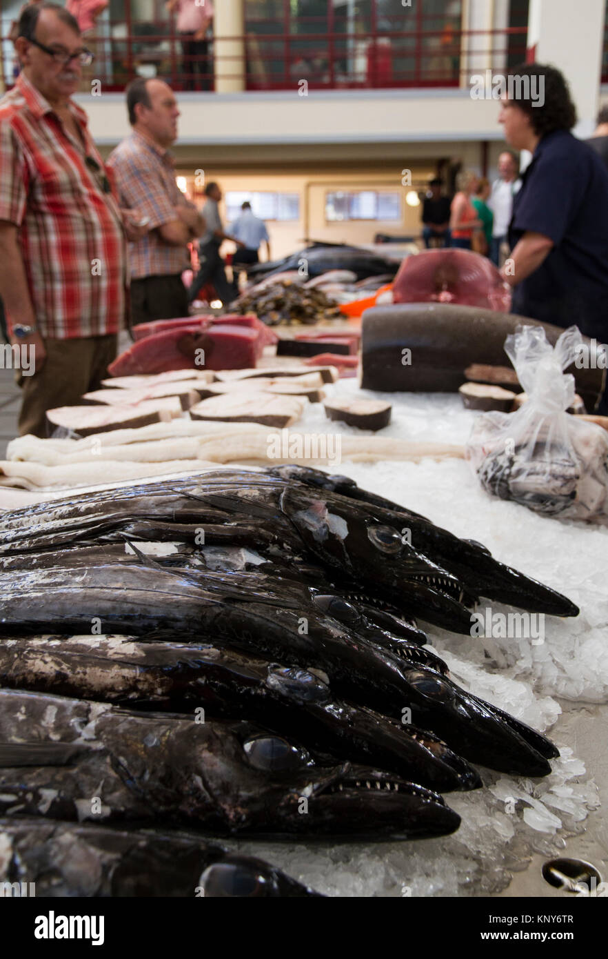 Vendors and buyers trading fish inside the farmers market of Funchal Madeira with close-up view of espada fish Stock Photo